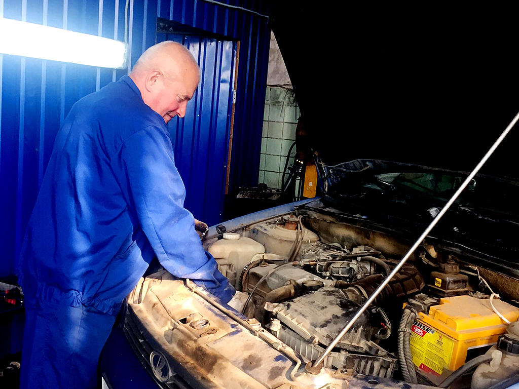 На фото мастер автосервиса выполняет ремонт двигателя автомобиля отечественного производства.